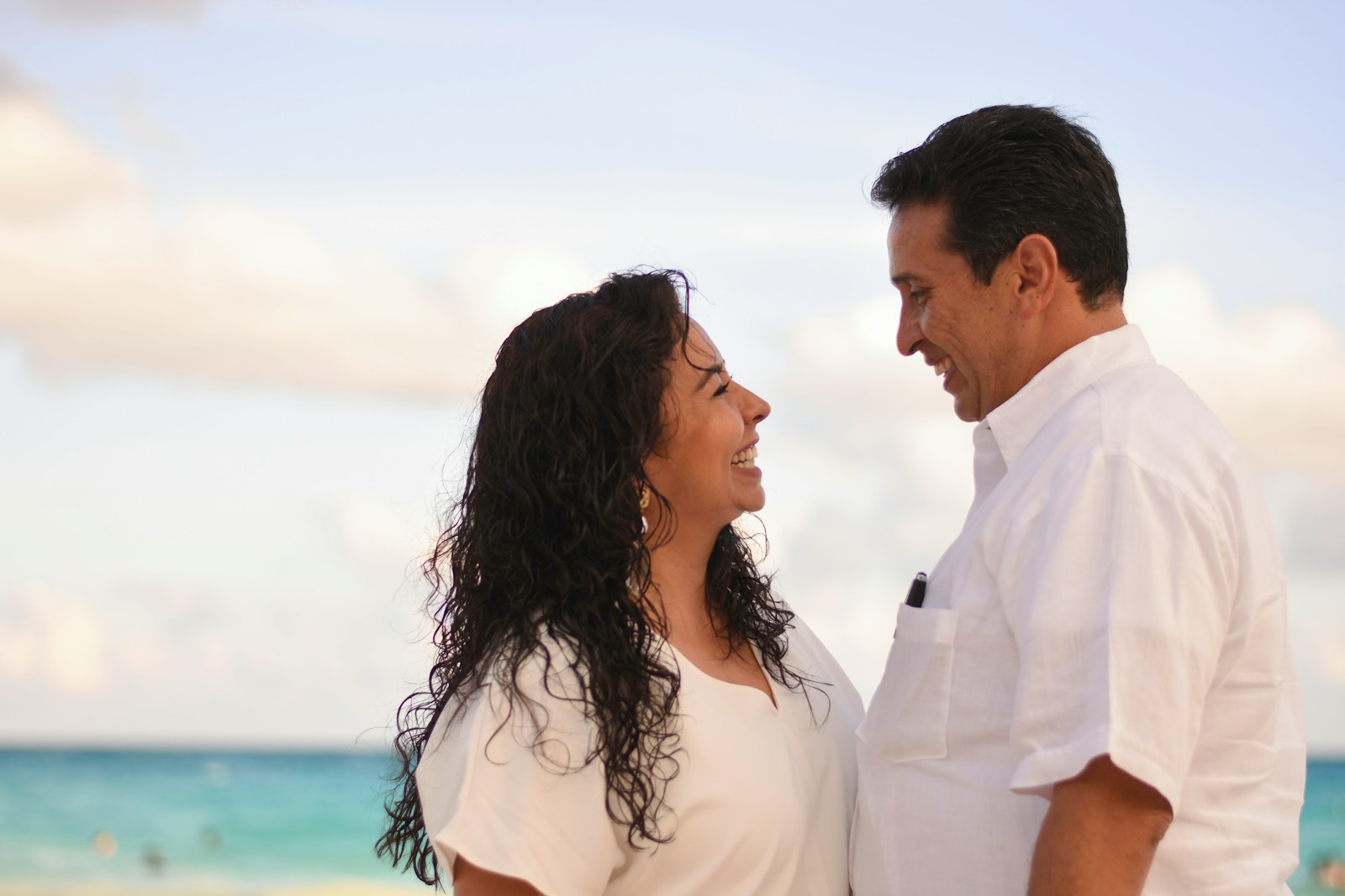 man and woman facing each other while smiling at the beach